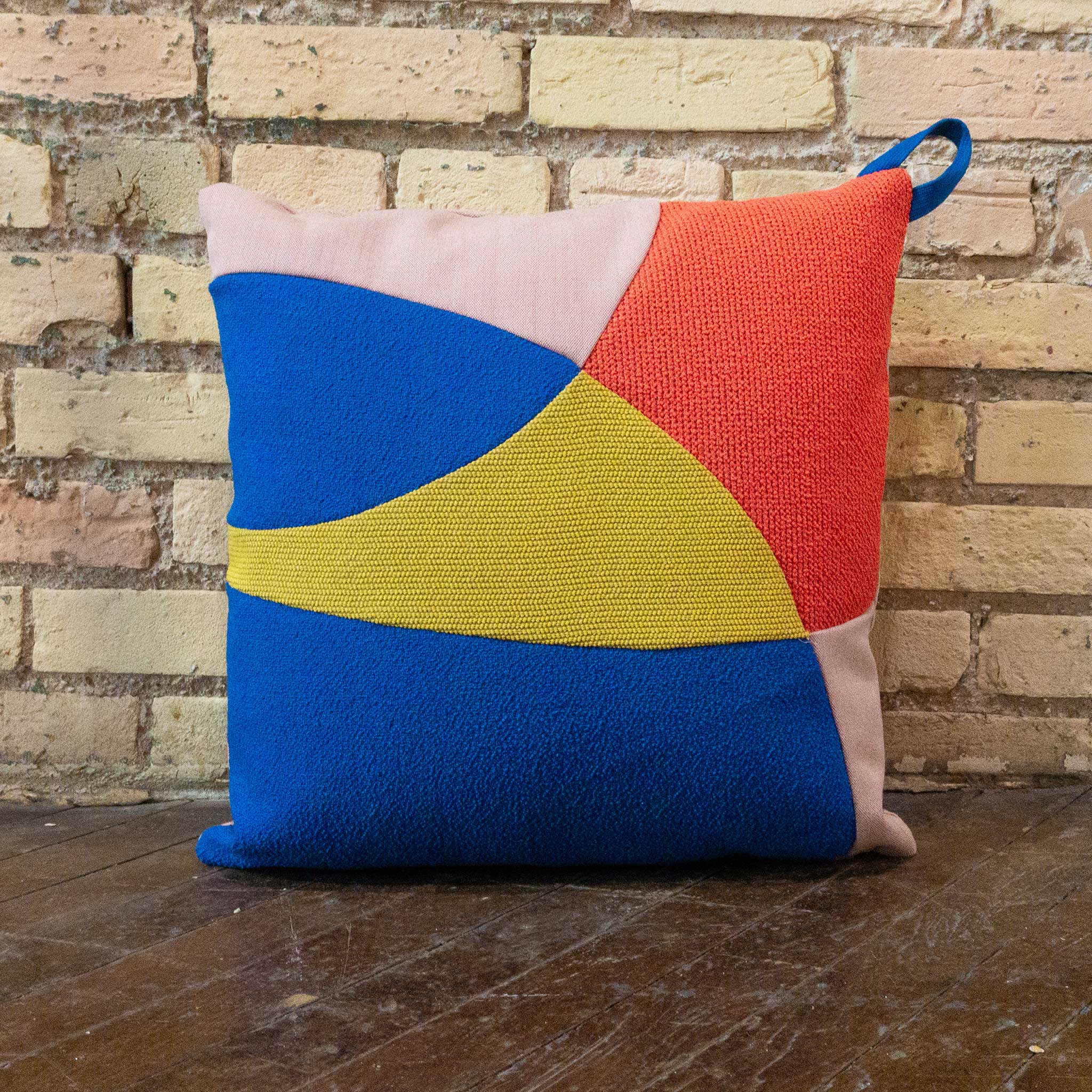 Colorful geometric pillow on a wooden surface with a brick wall background