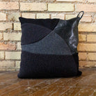 Black pillow with geometric pattern against a brick wall.