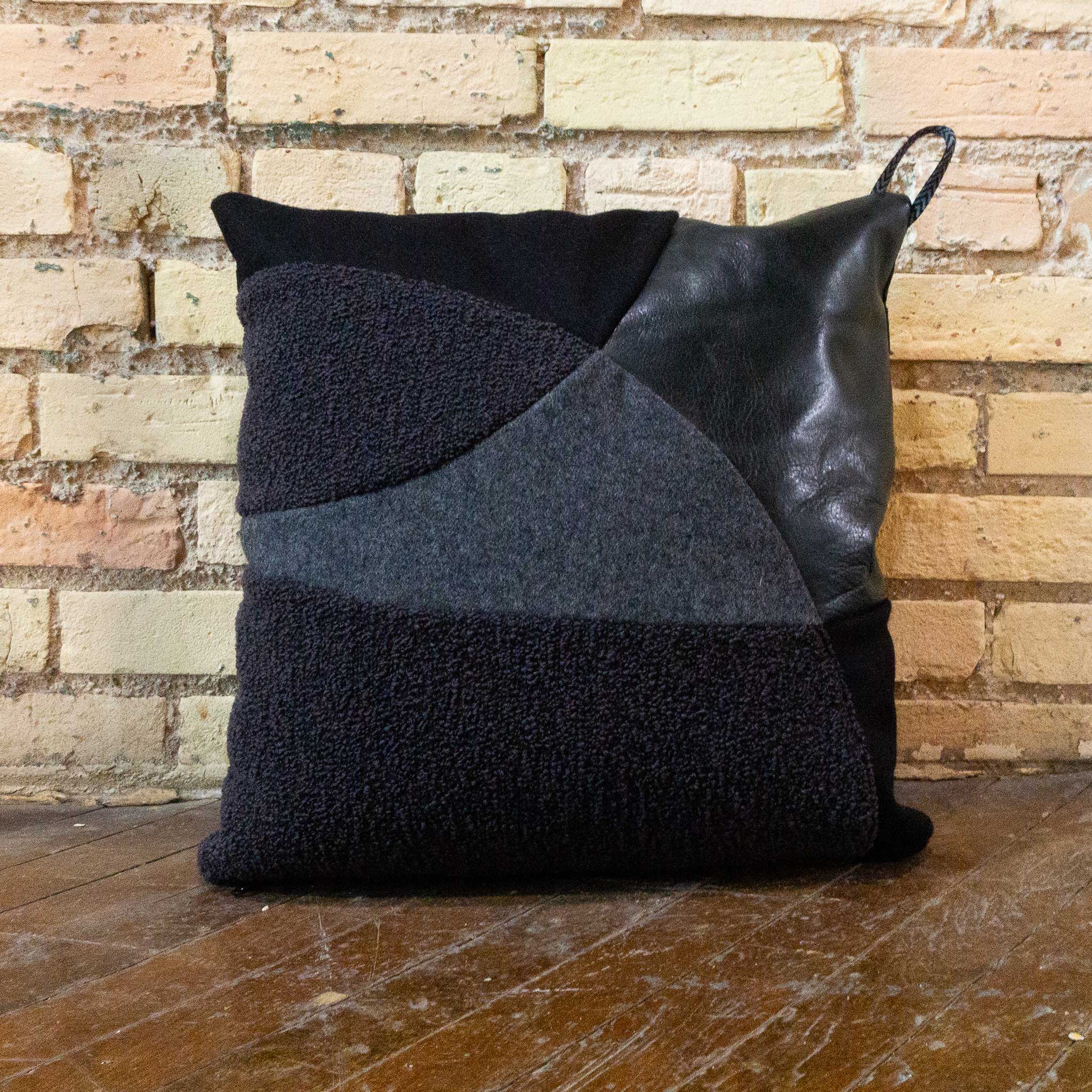 Black pillow with geometric pattern against a brick wall.