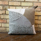 Patchwork pillow with geometric pattern against a brick wall.