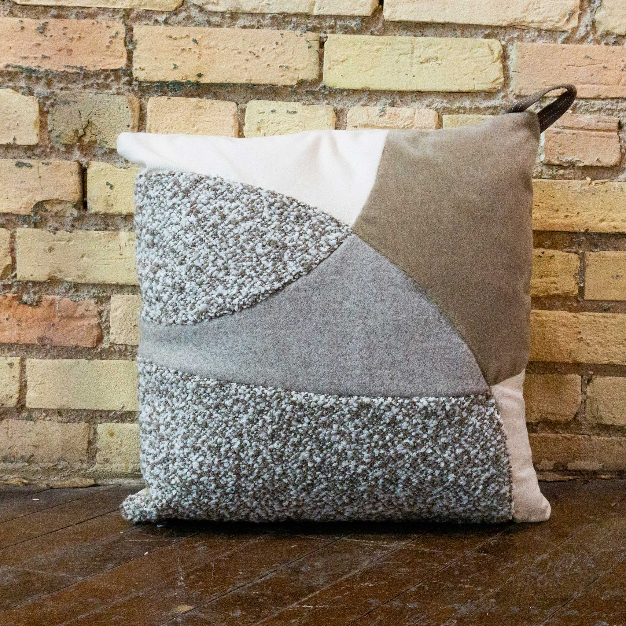 Patchwork pillow with geometric pattern against a brick wall.