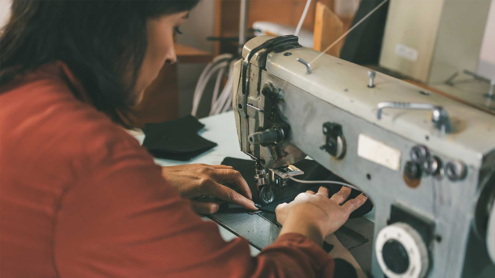 Women operating an industrial sewing machine in a workshop setting.